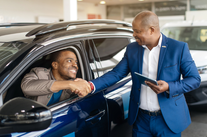 Car dealer shaking hand with a man sitting in a car.