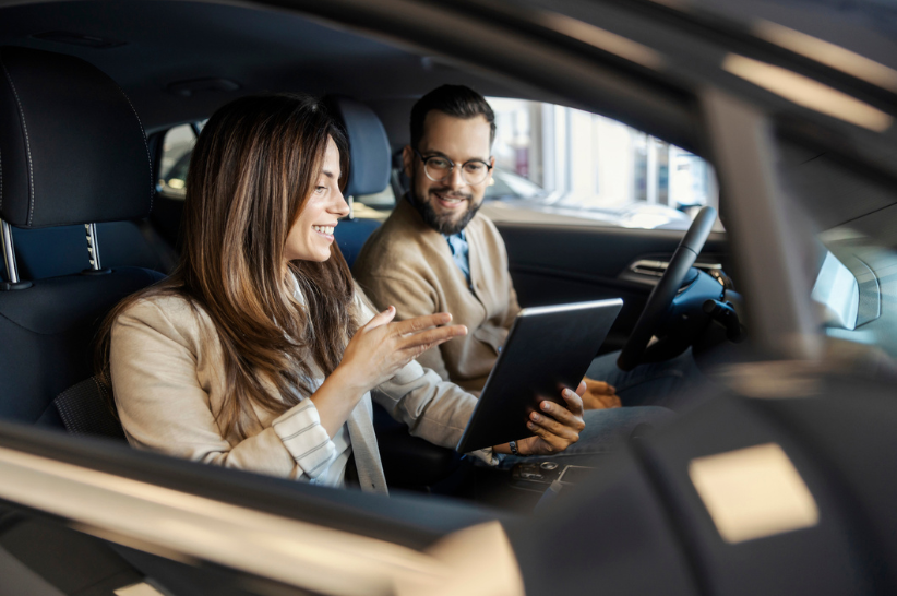Woman and Man sitting inside a car looking at an IPAD.