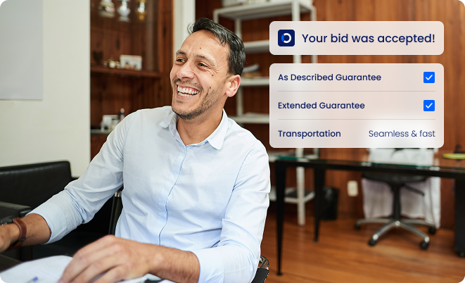 A man smiling at a desk with a notification onscreen reading Your bid was accepted! and checkmarks next to As Described Guarantee, Extended Guarantee, and Transportation: Seamless & fast.